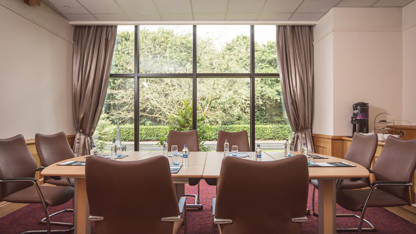 Elegant meeting room with large window view of green garden, featuring comfortable leather chairs and a refreshment station.