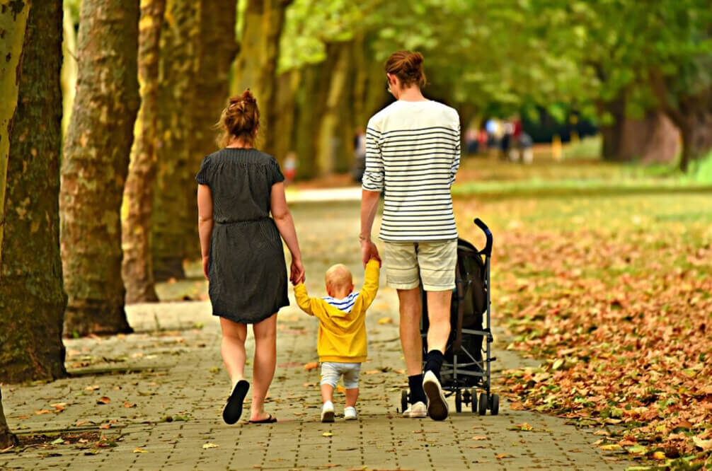 Family strolls under lush trees in hotel garden. Enjoy peaceful walks and serene nature views, perfect for a relaxing stay.