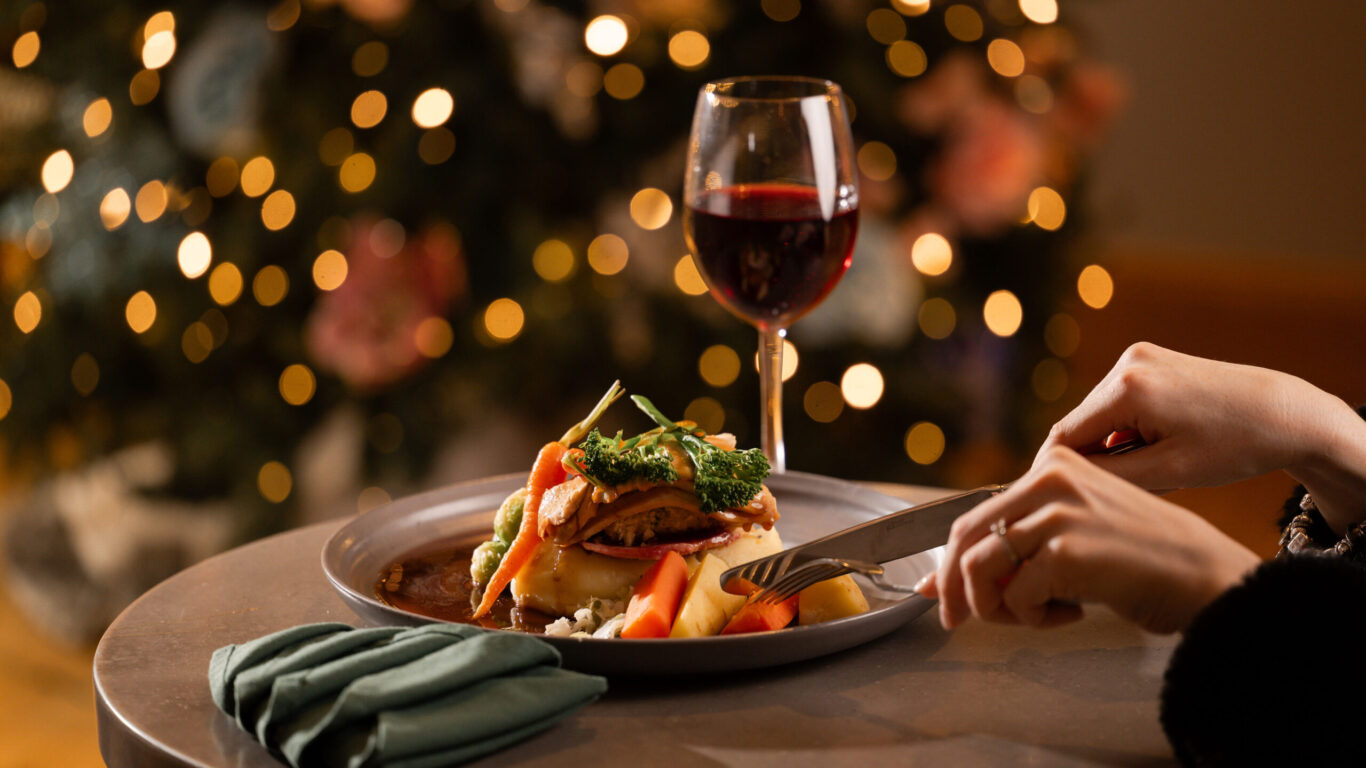 Elegant dining with gourmet dish and wine, festive bokeh lighting, enhancing a joyous hotel restaurant experience.