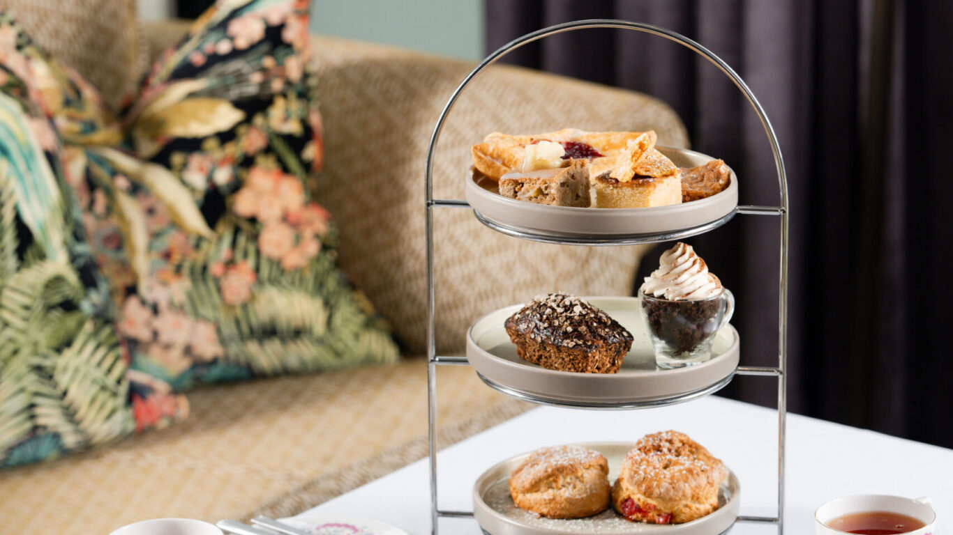 Afternoon tea setup with tiered tray, scones, pastries, and tea on elegant tableware in cosy hotel lounge.