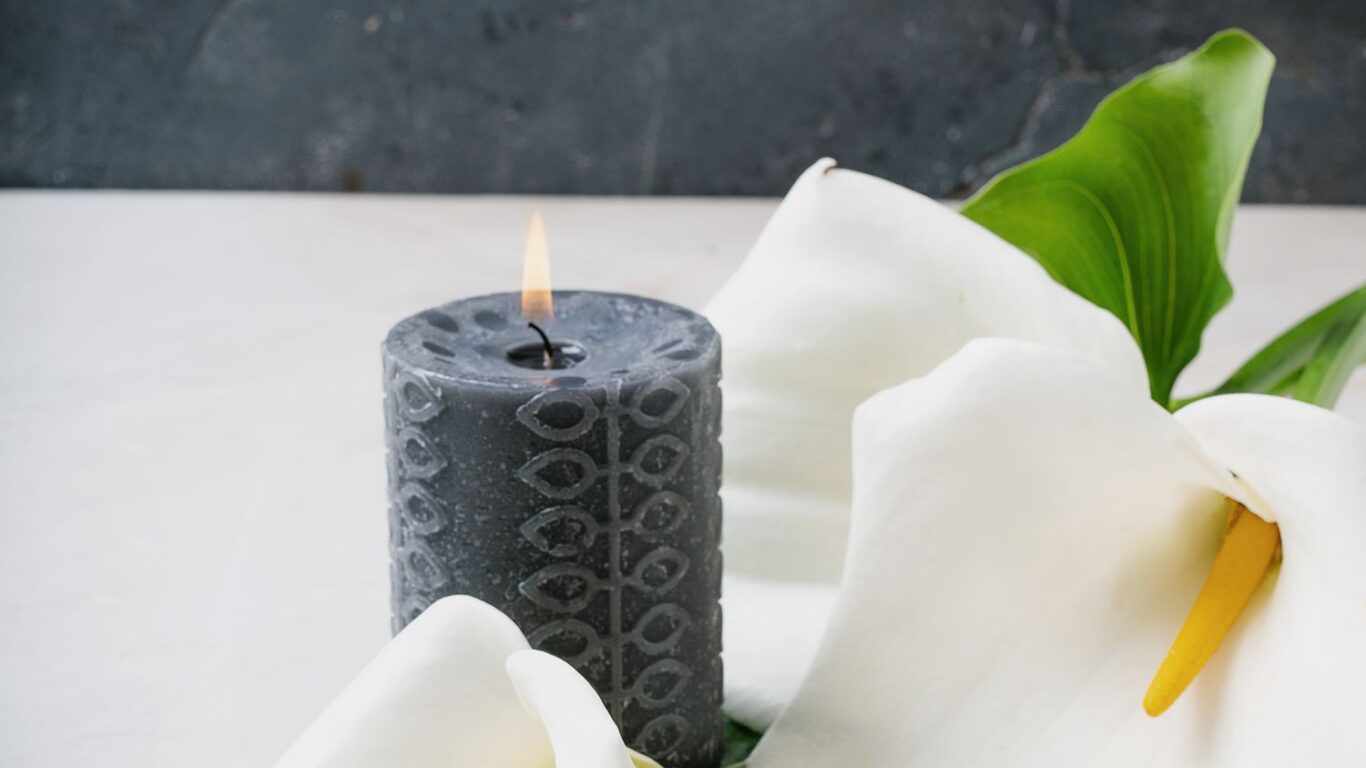 Elegant spa scene with textured black candle and white lilies, offering a tranquil hotel retreat experience.